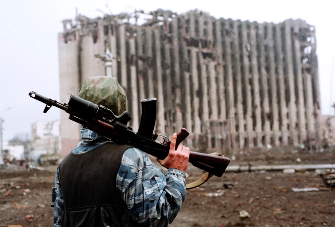 Боец с автоматом на плече стоит недалеко от разрушенного президентского дворца.